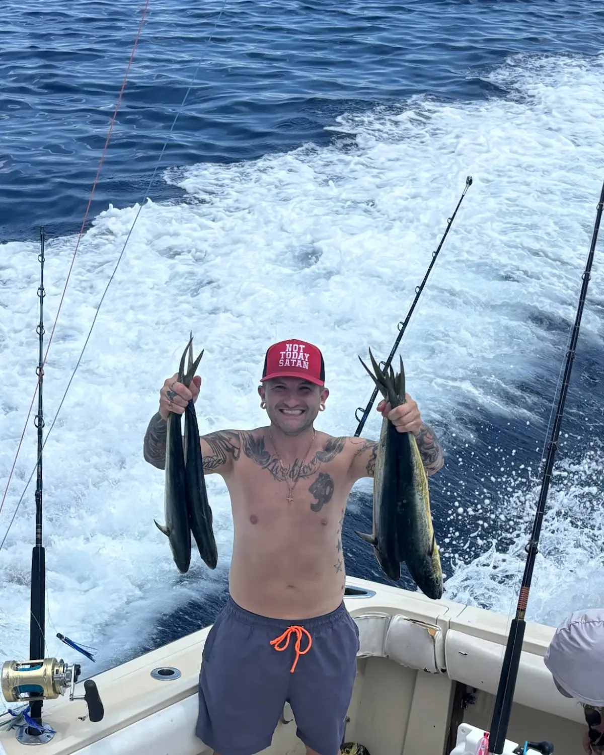 An angler holding up two kingfish on the back deck as the boat runs in