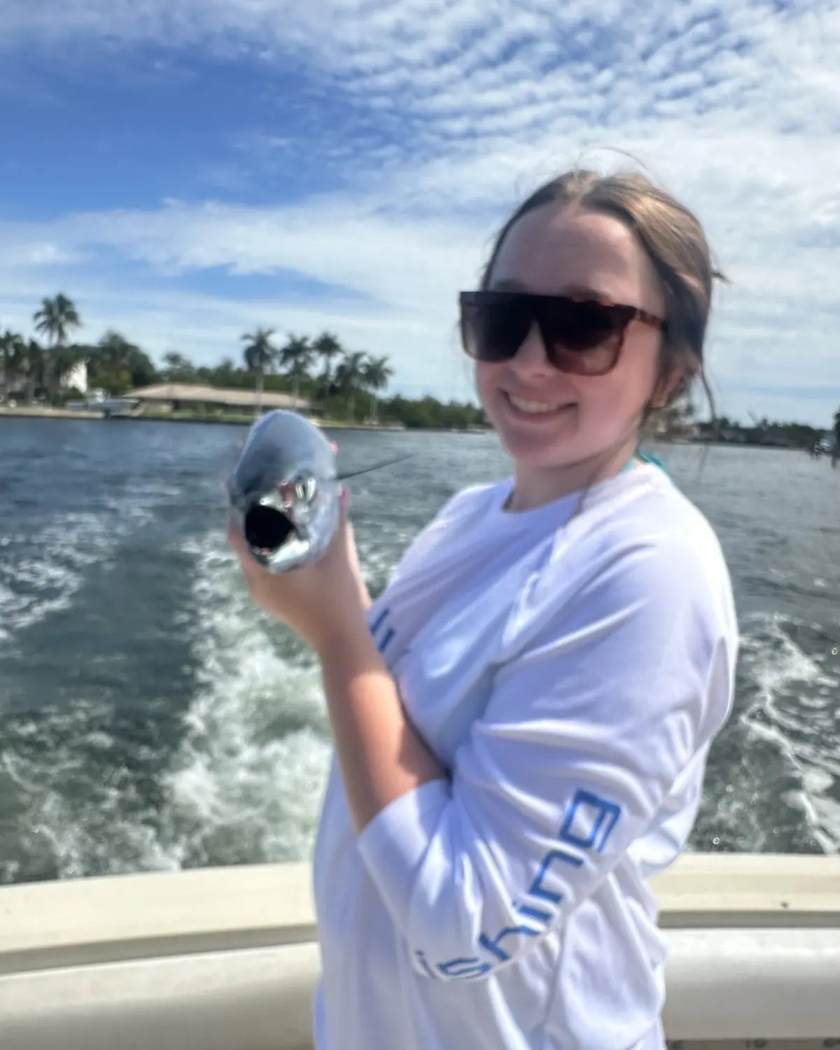A guest in a sun shirt holding her first fish as the boat runs down the Intracoastal