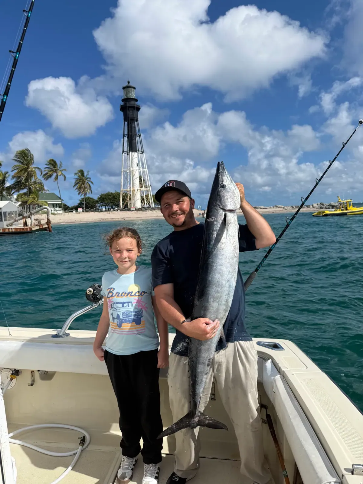A young angler and the mate holding a wahoo taller than she is, the Hillsboro lighthouse behind
