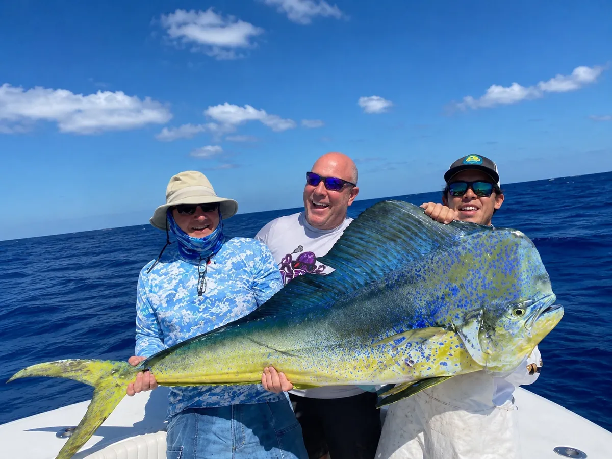 Three anglers holding a big bull mahi across the cockpit in the blue water off Pompano Beach