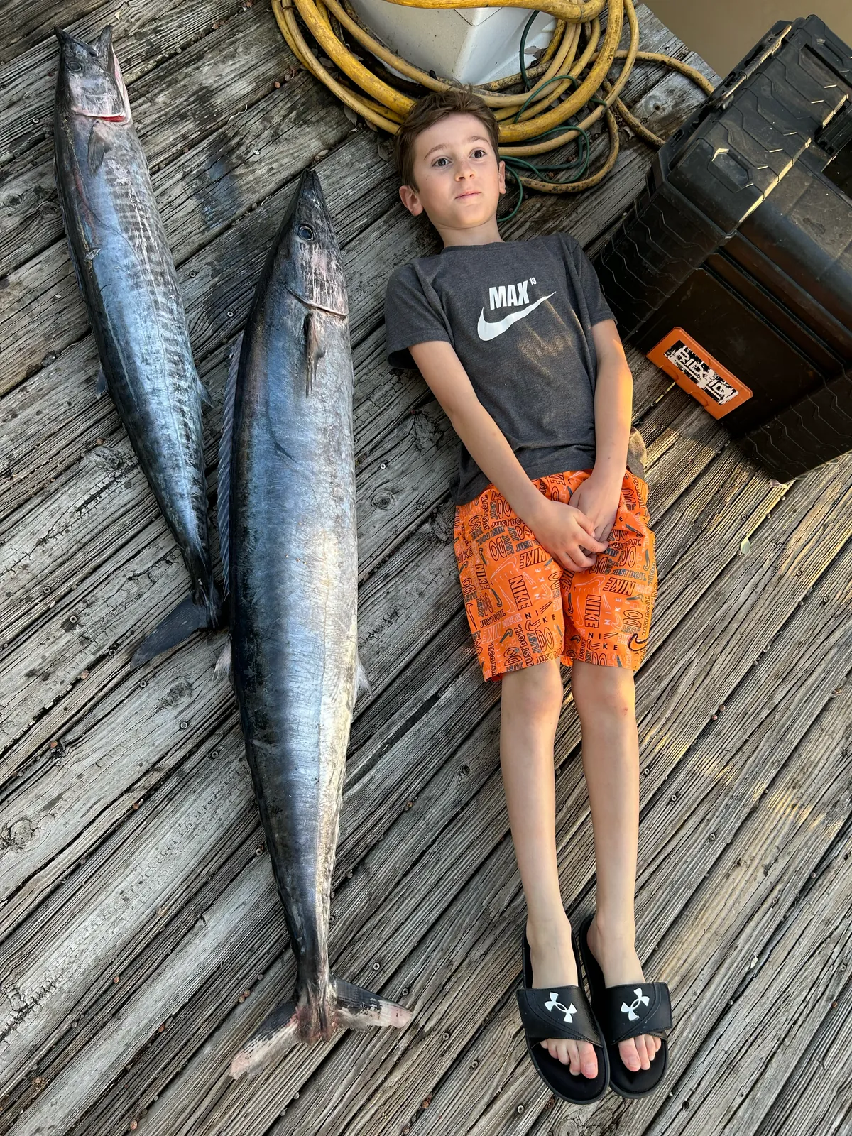 A young angler on the dock beside two wahoo, each longer than he is tall